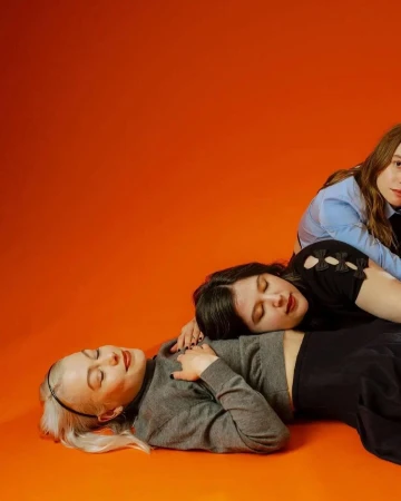 Three women posing against a solid orange background, styled by fashion stylist Lindsey Hartman