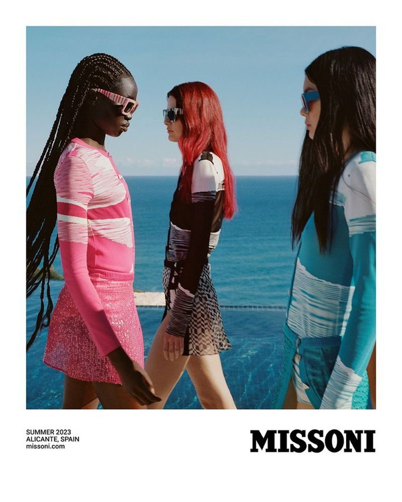 Three fashion models in sunglasses and colorful knitwear walk along a terrace overlooking the ocean in a vibrant outdoor setting for Missoni.