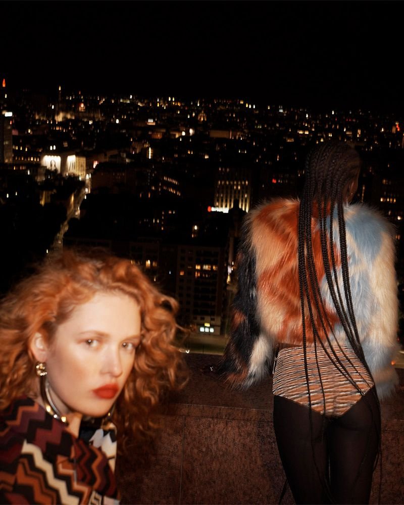 Two models on a rooftop at night with city lights in the background styled by Lorenzo Posocco in Milan.