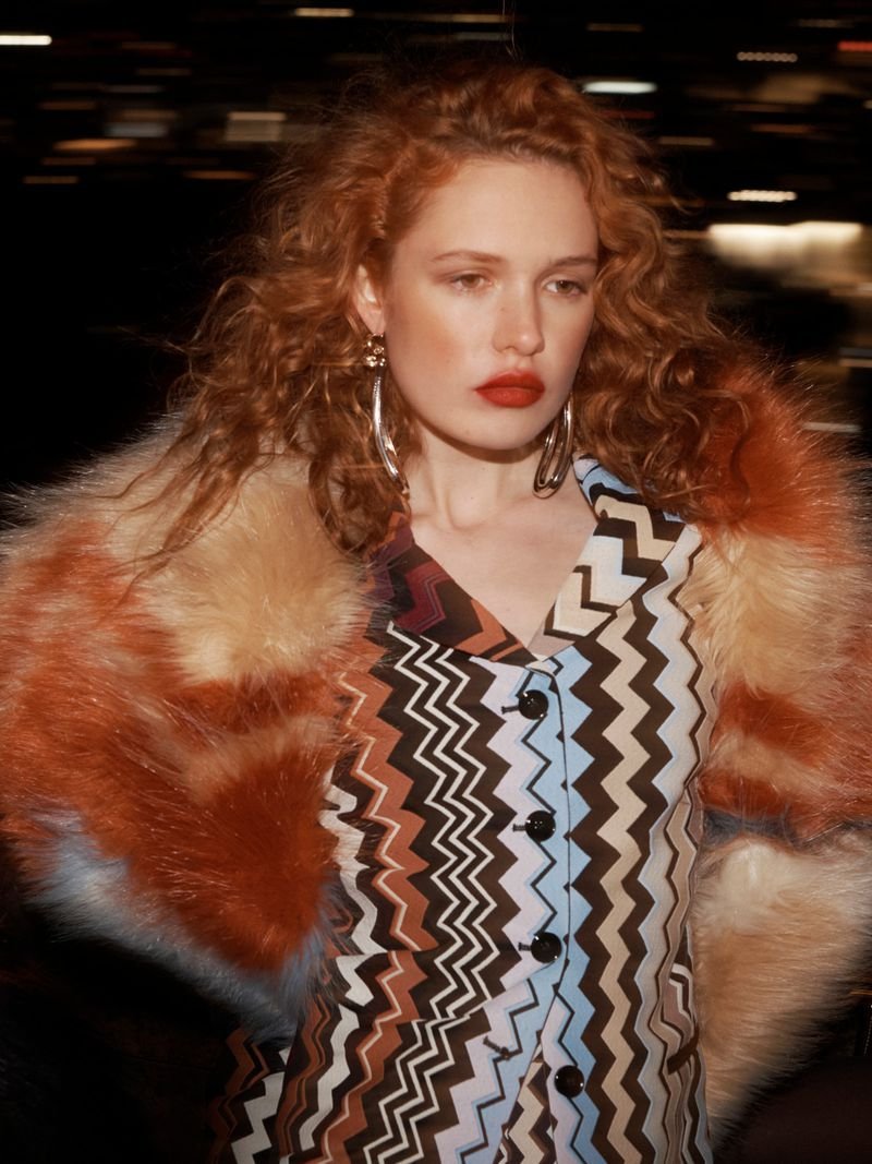 Red-haired model wearing a zigzag-patterned buttoned top and furry coat, styled by Lorenzo Posocco.