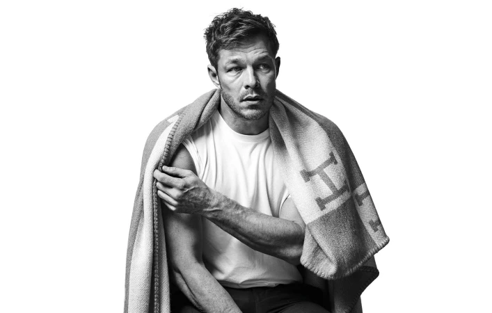Man wearing a white t-shirt draped in a patterned blanket against a white background
