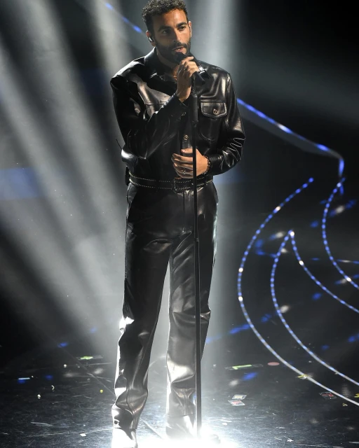 Singer in a leather outfit performing on stage with a microphone under bright spotlights, creating a dramatic and captivating atmosphere.