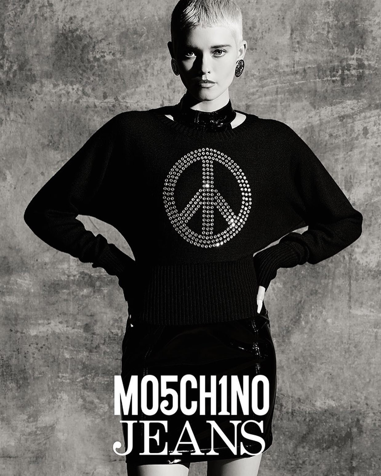 Black-and-white studio portrait of a young adult woman wearing a peace-symbol sweater and black mini skirt in a fashion shot.