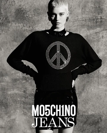Black-and-white studio portrait of a young adult woman wearing a peace-symbol sweater and black mini skirt in a fashion shot.