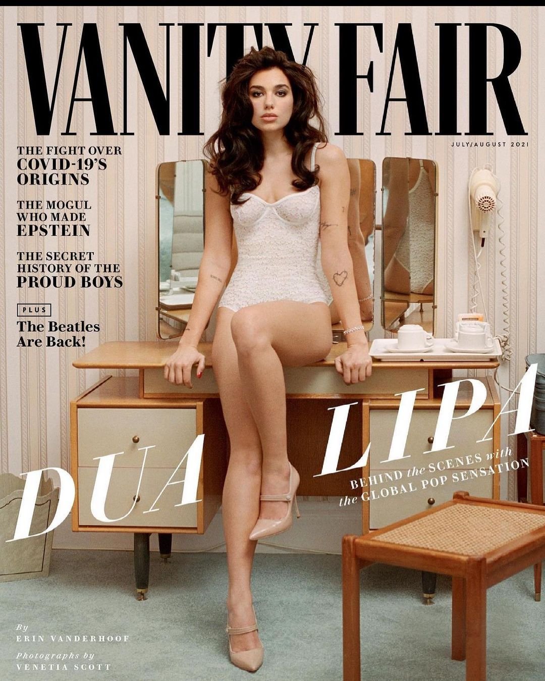 Vanity Fair cover featuring Dua Lipa in a white lace corset and nude heels, posing on a desk in a retro-style room.