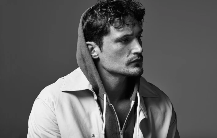 Portrait of a man in profile wearing a zipped jacket over a hooded sweatshirt styled by Lorenzo Posocco.