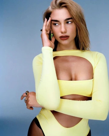 Portrait of Dua Lipa wearing a yellow cutout top and dark tights against a plain grey background