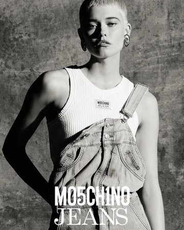 Black and white portrait of a model with short blonde hair wearing denim overalls and a ribbed tank top