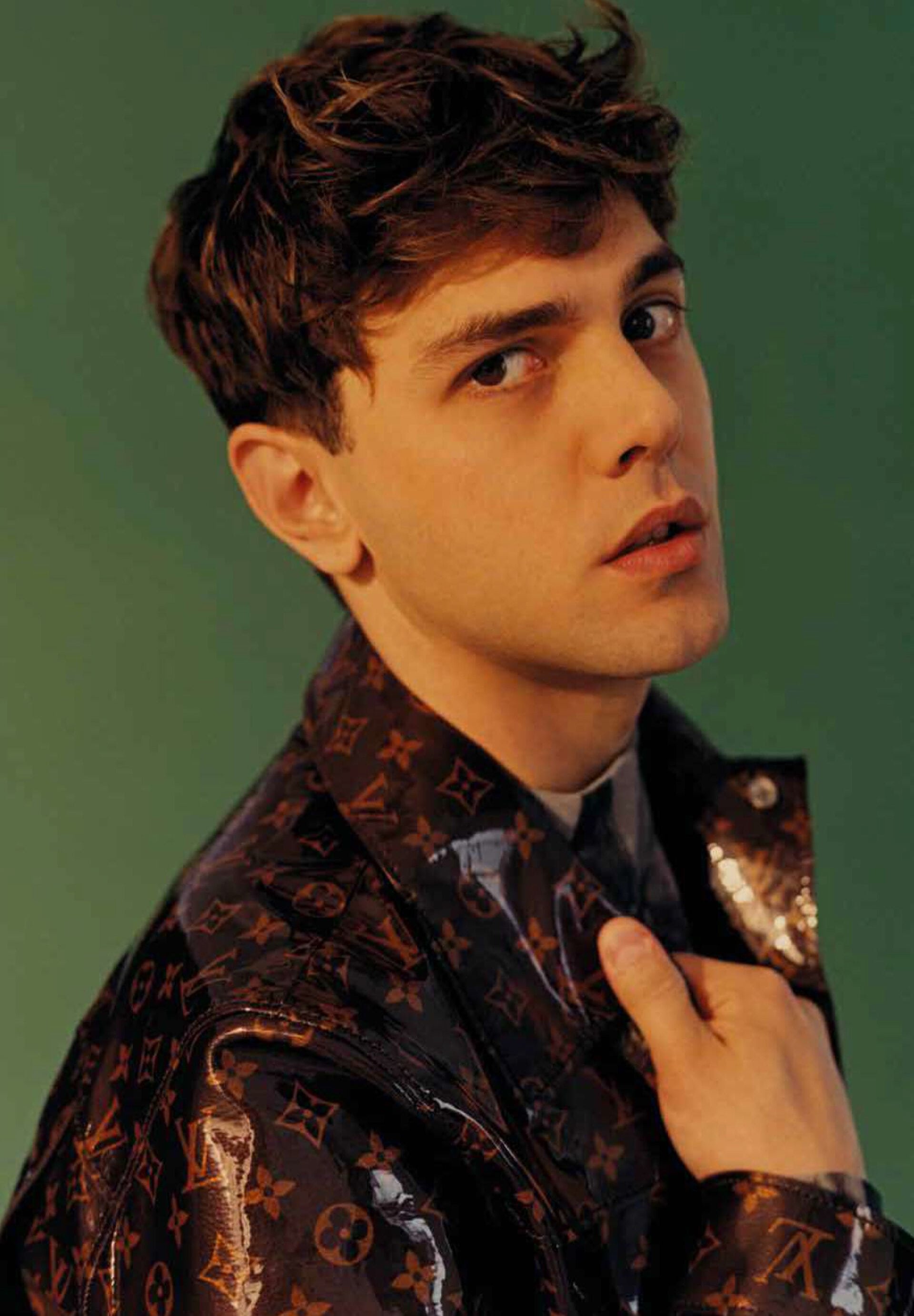 Portrait of a man in a glossy dark brown monogram jacket against a solid green background, styled by Lorenzo Posocco in Milan.