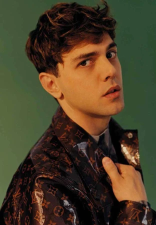 Portrait of a man in a glossy dark brown monogram jacket against a solid green background, styled by Lorenzo Posocco in Milan.