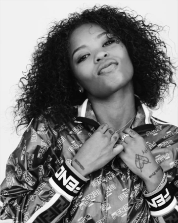 Monochrome portrait of a woman with curly hair wearing a branded zip jacket against a plain background.