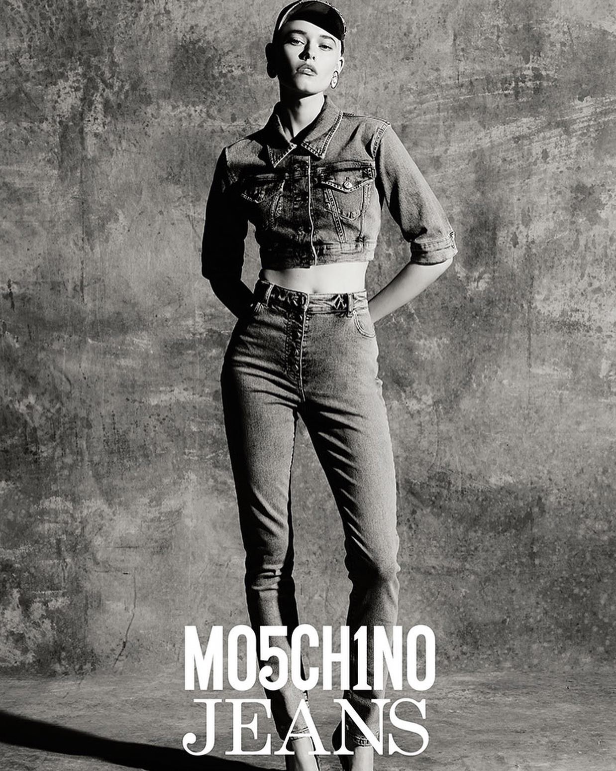 Model in denim jacket and high waisted jeans against a textured concrete background with bold white typography at the bottom.