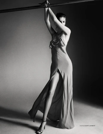 Model in a long slip dress with a thigh-high slit holding onto an overhead bar in a monochrome studio setting styled by Lorenzo Posocco.