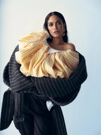 Model with dark wet-look hair wearing a voluminous yellow striped top and wrapped in a dark pinstripe coat.