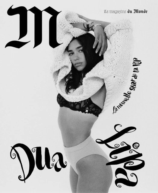 Black and white magazine cover shot of a woman wearing a knit sweater and underwear, posing in front of a white background.