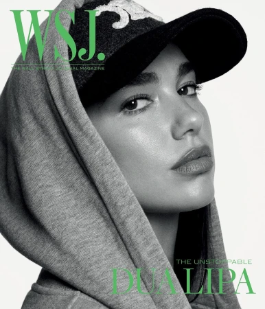 Close-up of Dua Lipa on a magazine cover, wearing a baseball cap and grey hooded sweatshirt against a bright white background.