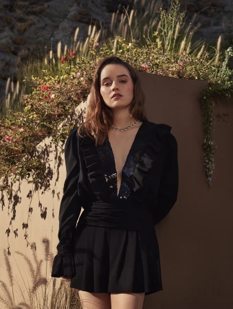 Woman in a black plunging V-neck dress standing against an outdoor concrete wall with planter boxes in Milan