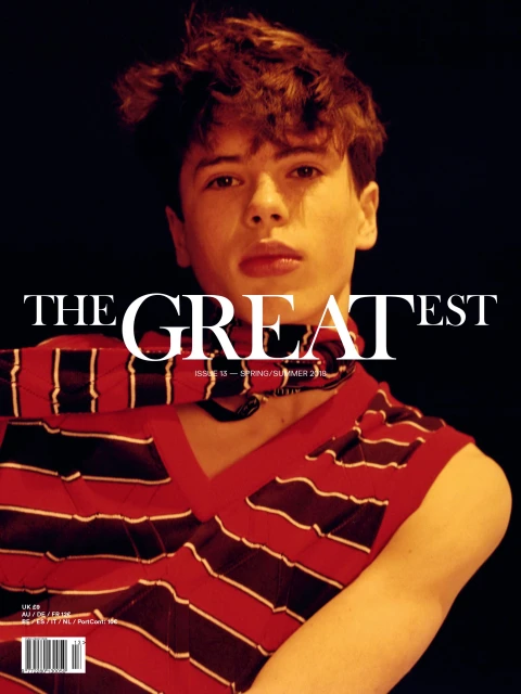 Magazine cover featuring a young male model with dark hair, wearing a striped top, set against a dark backdrop with bold white text.