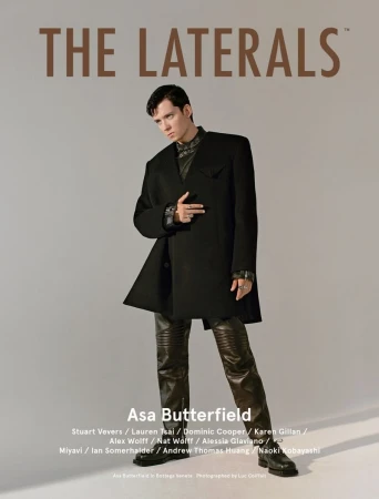 Asa Butterfield poses in a black coat and leather pants against a grey backdrop, featured on the cover of The Laterals magazine.