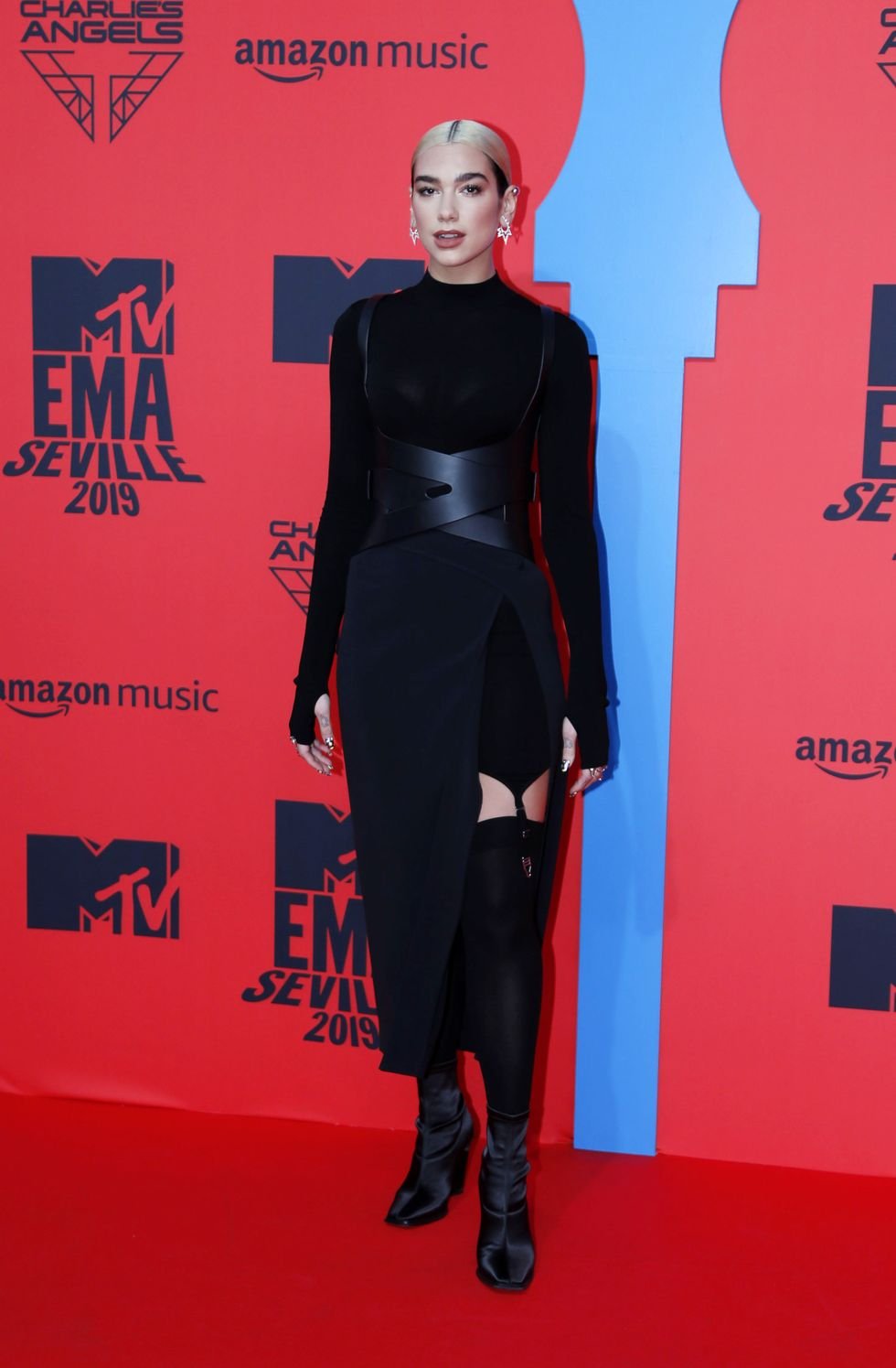 Dua Lipa poses on a red carpet in a black dress and boots at the MTV Europe Music Awards in Seville, Spain, in 2019.