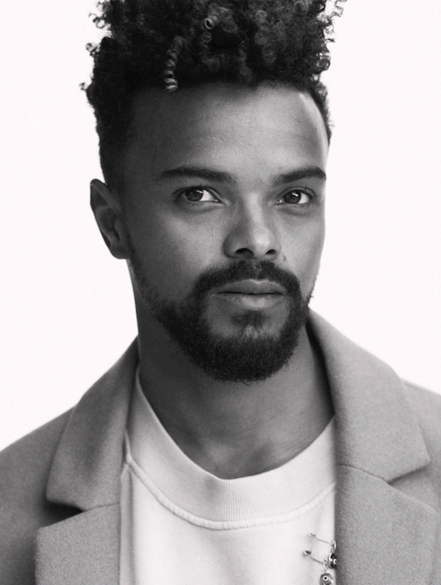 Portrait of handsome African-American male model in a light coat, wearing a white sweatshirt, shot in a photo studio on a white background.