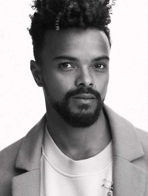 Portrait of handsome African-American male model in a light coat, wearing a white sweatshirt, shot in a photo studio on a white background.