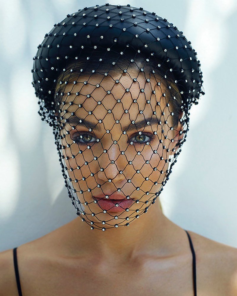 Close-up of a woman wearing a jeweled black headpiece and net veil, showcasing fashion and beauty with elegant accessories.