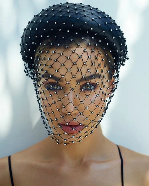Close-up of a woman wearing a jeweled black headpiece and net veil, showcasing fashion and beauty with elegant accessories.