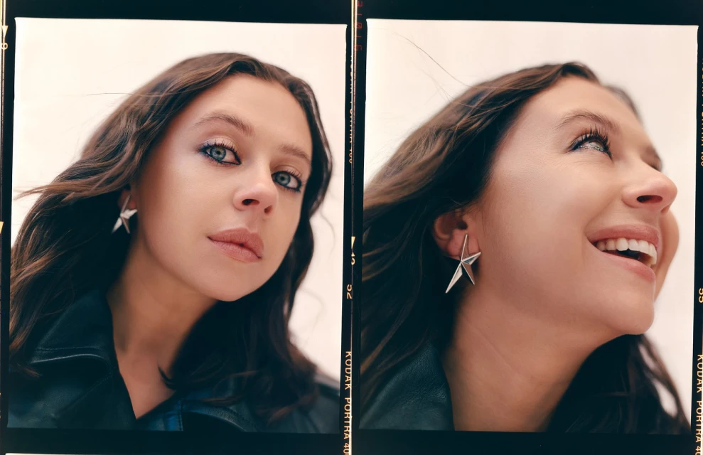 Close-up of a woman with brown hair wearing a black jacket and star earrings, in a studio-lit portrait showcasing beauty and fashion.