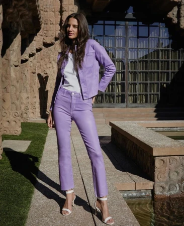 Woman in lilac jacket and matching pants standing outdoors near textured stone columns styled by Lucy Warren