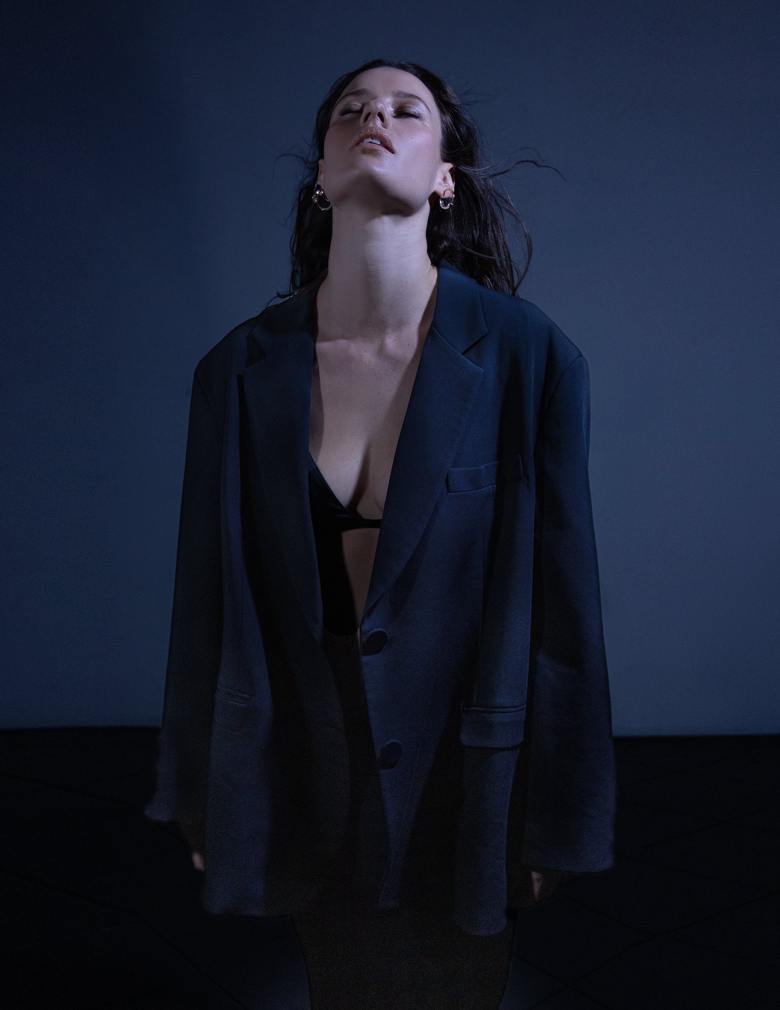 Portrait of a young woman wearing a blazer and bra top in a studio with blue lighting, showcasing fashion and portrait photography.
