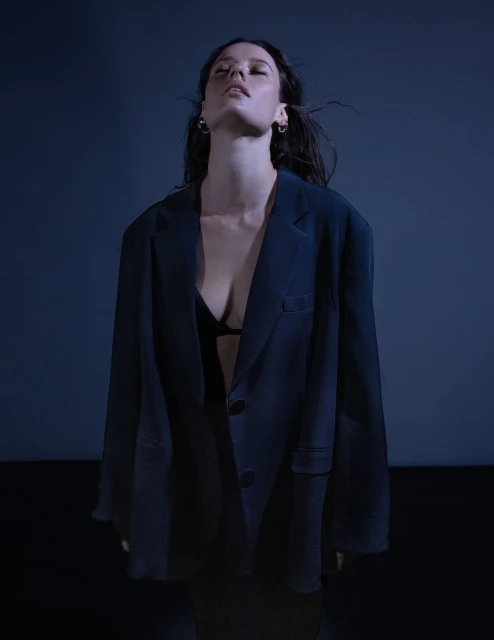 Portrait of a young woman wearing a blazer and bra top in a studio with blue lighting, showcasing fashion and portrait photography.