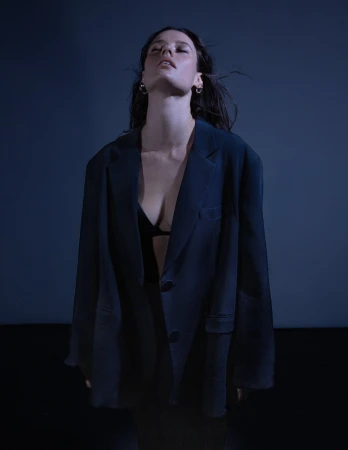 Portrait of a young woman wearing a blazer and bra top in a studio with blue lighting, showcasing fashion and portrait photography.