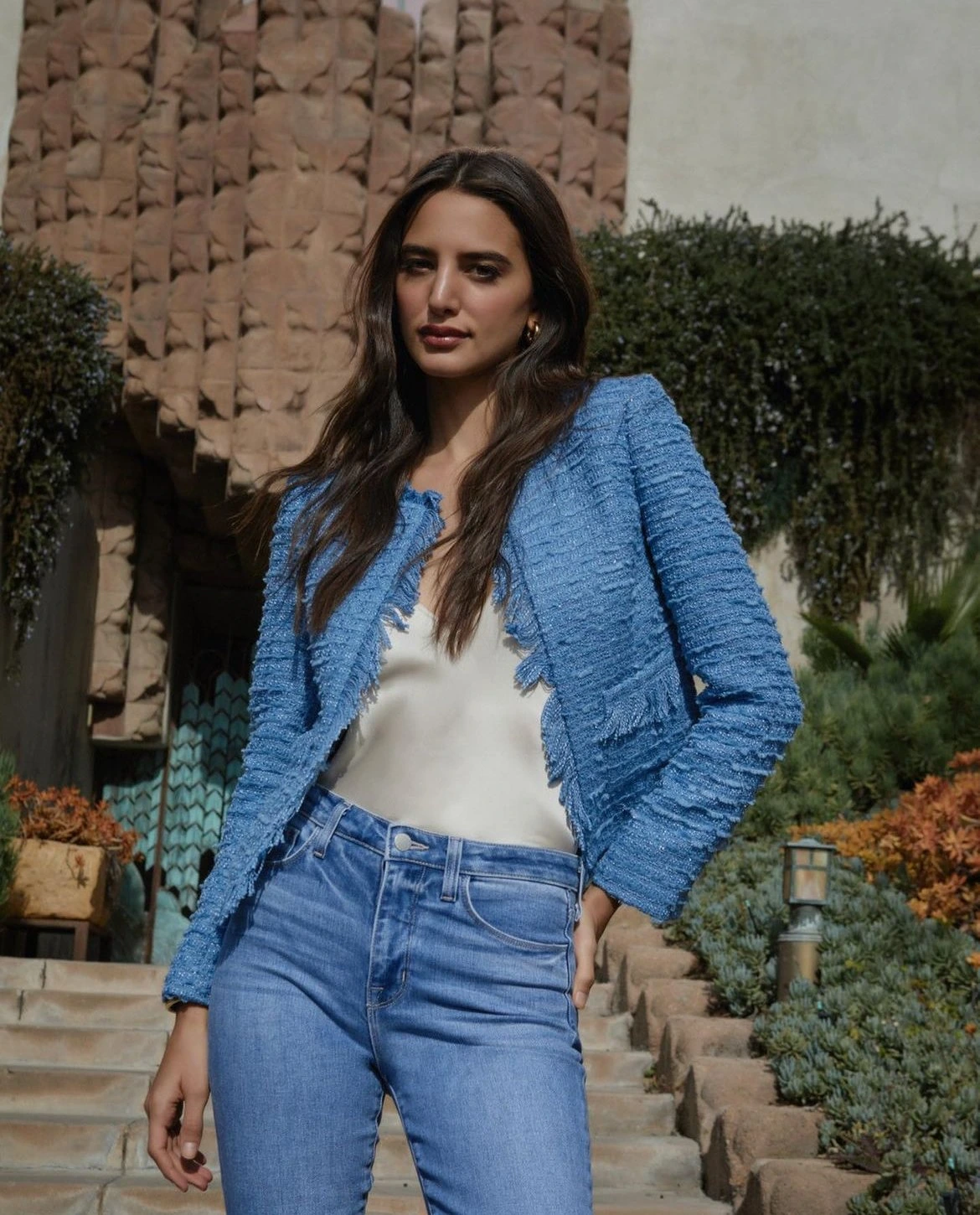 Woman in a textured blue tweed jacket and jeans standing outdoors on stone steps