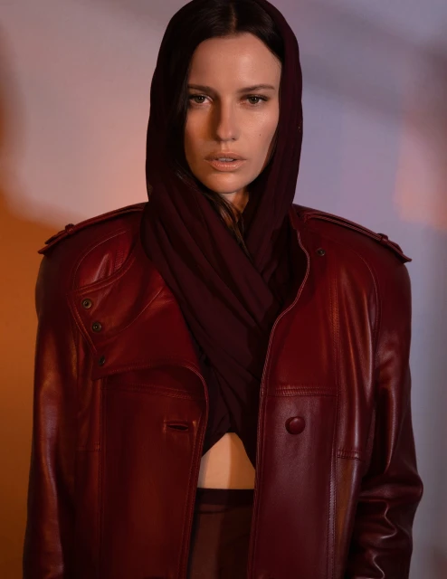 Portrait of an adult woman wearing a burgundy leather jacket and hooded top, posing in a photo studio with soft lighting.