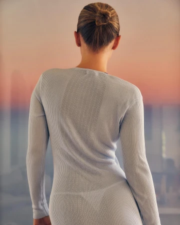 Back view of a fair-skinned adult woman with a high bun, wearing a form-fitting, long-sleeved dress against a blurred background. 