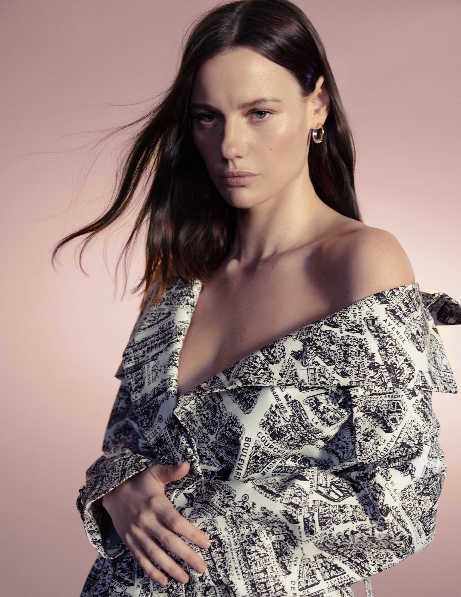 Portrait of a brunette woman wearing hoop earrings and a black and white jacket against a gradient peach background.