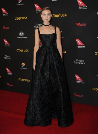 Woman in black gown on red carpet at G'Day USA event. Evening light, formal wear, celebrity appearance, black dress, red carpet, event backdrop.
