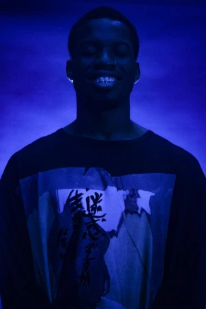 Black man with closed eyes smiling wearing a graphic t-shirt under moody blue lighting in Los Angeles