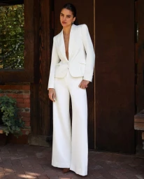 Woman wearing a matching white blazer and wide leg trousers standing before dark wooden doors styled by Lucy Warren