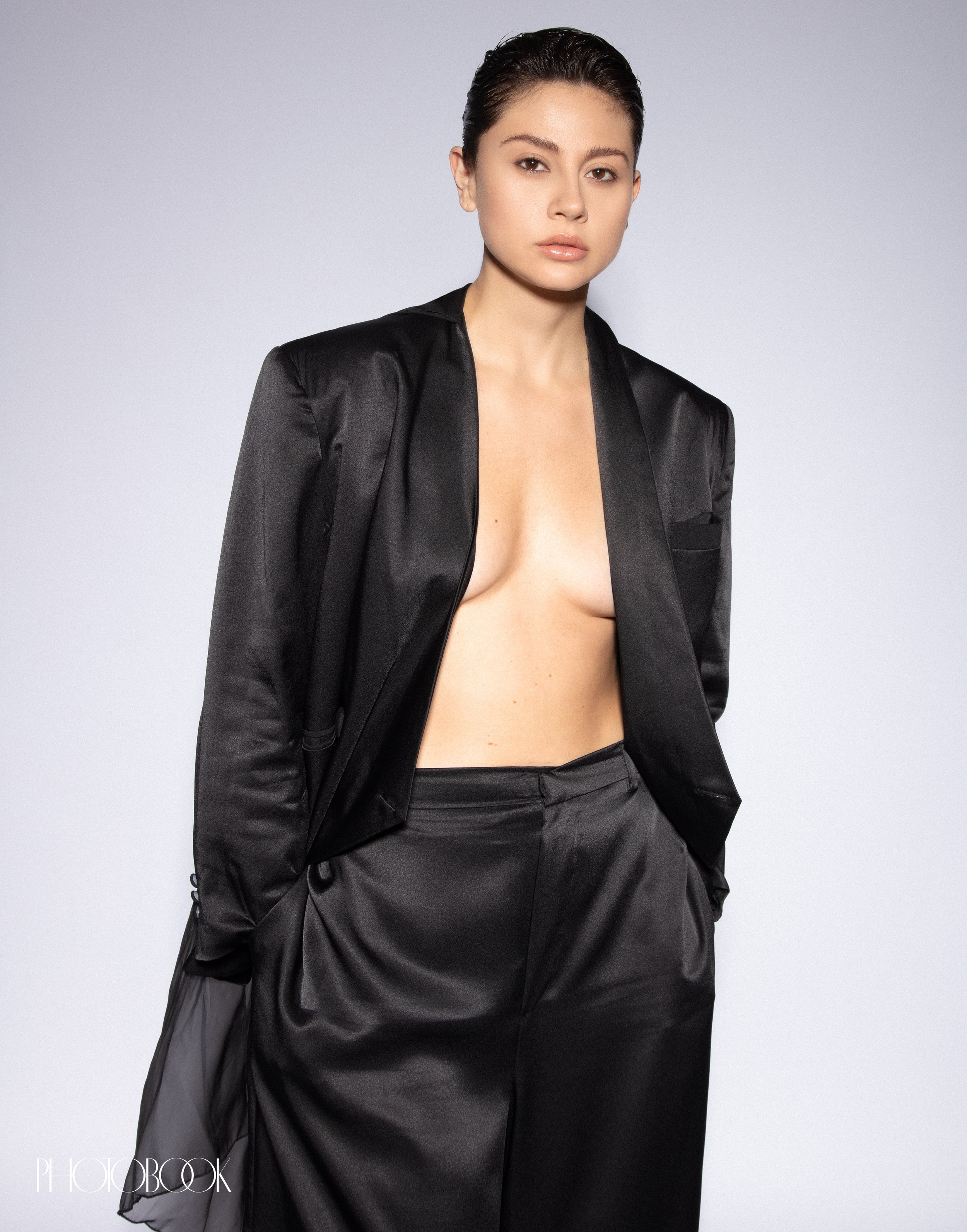 Portrait of a woman in a black silky suit and bare chest against a white background in a studio. Fashion and beauty shot.