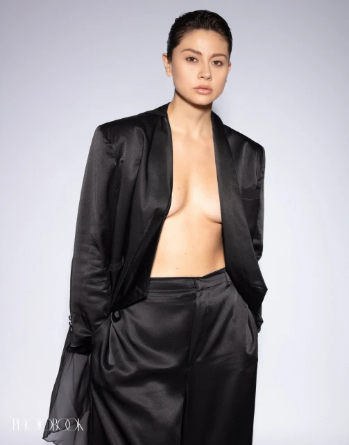 Portrait of a woman in a black silky suit and bare chest against a white background in a studio. Fashion and beauty shot.