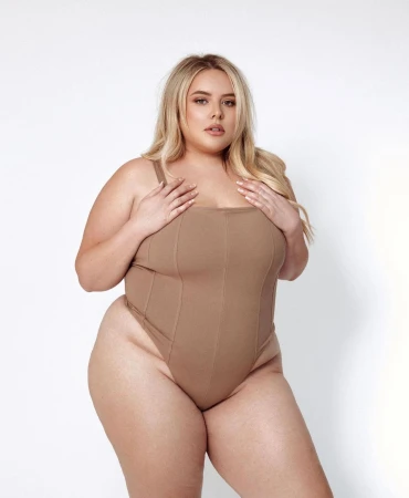 Plus size blonde woman wearing a beige bodysuit against a white studio background by Madison Clifford