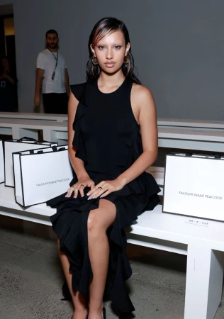 Woman in black ruffled dress seated on white bench with branded shopping bags in background