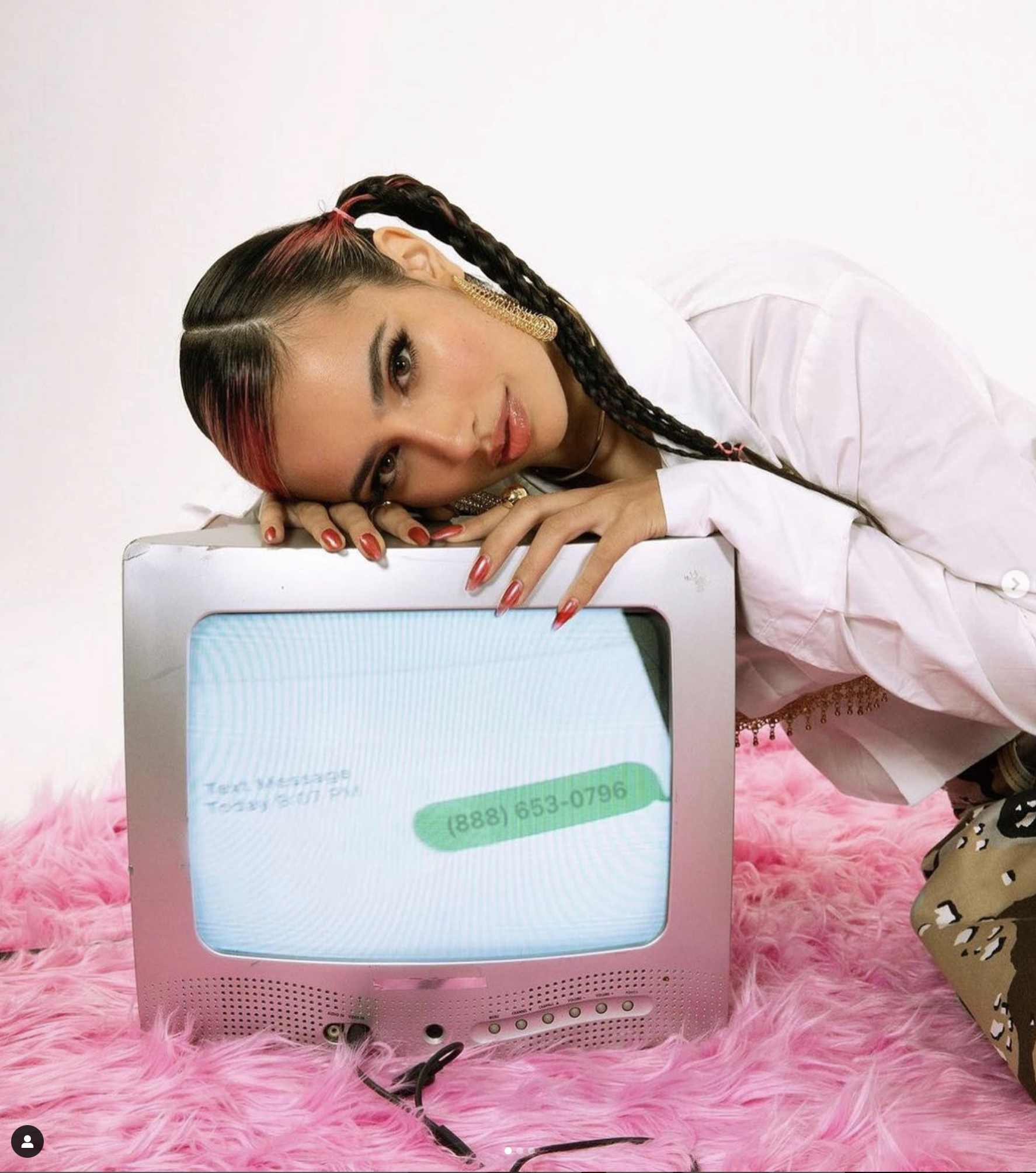 A woman with braided hair rests her head on a retro TV displaying a phone number against a white background and a pink fluffy rug.
