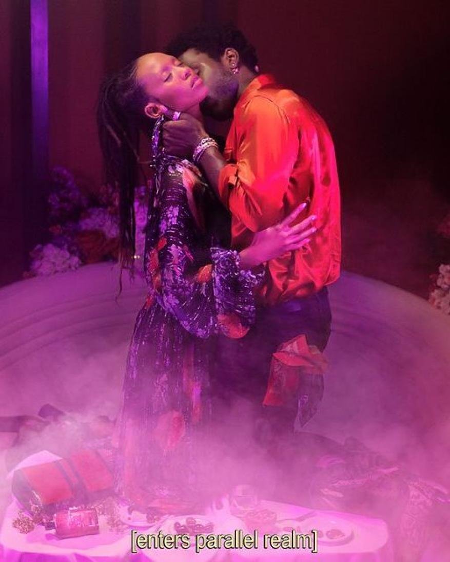 Intimate portrait of a couple in embrace, set in a dreamy, fog-filled space with vibrant floral arrangements and dramatic lighting.