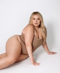 Plus size blonde model wearing a brown bodysuit posing against a clean white seamless studio background.