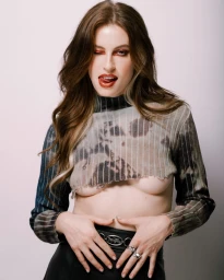 Woman wearing a cropped patterned sweater and black skirt sticking her tongue out against a light background