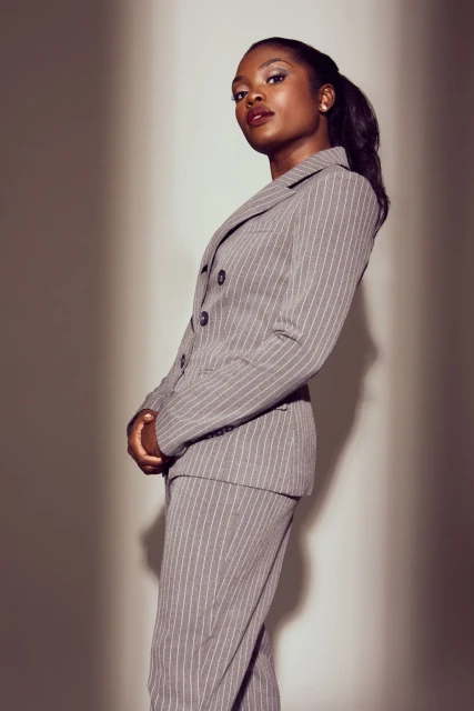 Portrait of a young Black woman in a stylish grey pinstripe pantsuit, posing indoors with a confident expression and soft lighting.