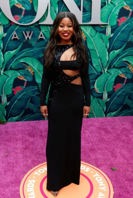 A woman on a purple carpet wearing a long, elegant black dress with sequined detailing and cut-out design at a Tony Awards event.